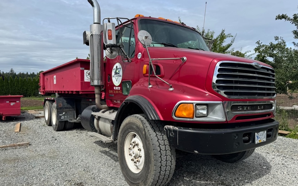 An Eric's Disposal truck hauling a red roll off bin, ready for delivery