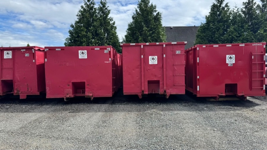 A row of Eric's Disposal bins at a job site, including one marked Drywall Only for a construction tear-out