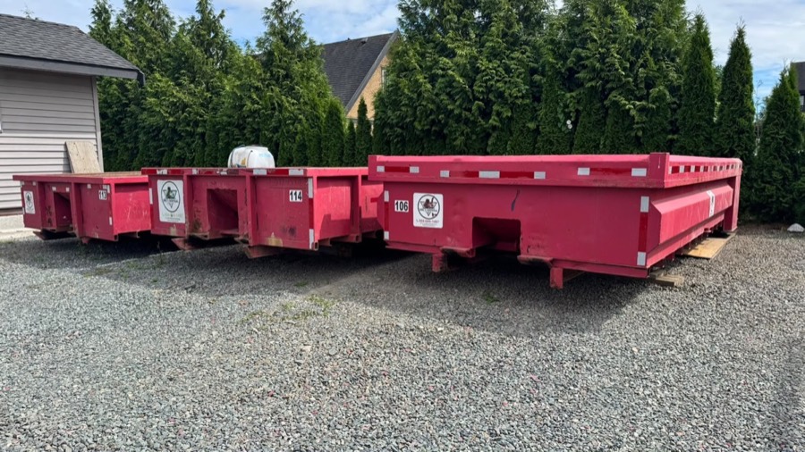 Three Eric's Disposal roll off bins staged in a residential driveway, houses visible behind the hedge